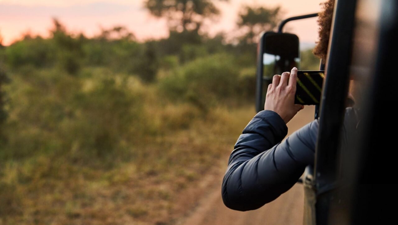 Young woman taking a smartphone photo from safari vehicle in wildlife reserve